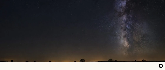 Céu noturno sobre um horizonte baixo, com a Via Láctea e um brilho quente junto à linha do horizonte.